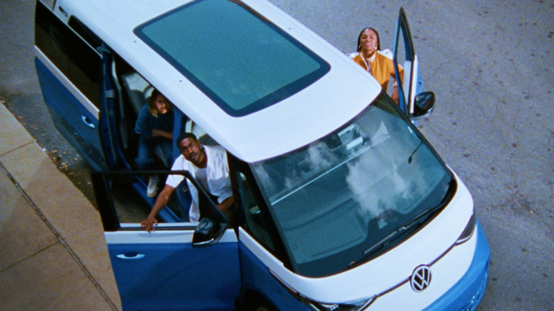 An  aerial view of three people looking at the camera while sitting in an ID.Buzz shown in Cabana Blue Metallic and Candy White.