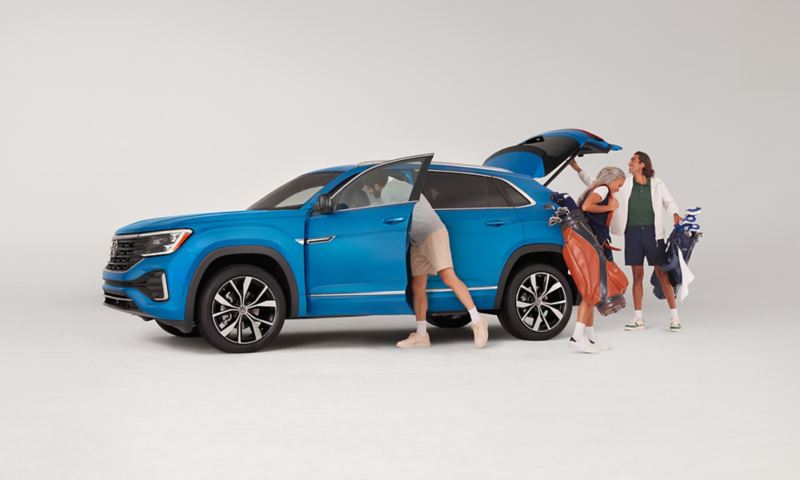Three people exit an Atlas Cross Sport shown in Kingfisher Blue Metallic parked on a white background with golf equipment in hand.