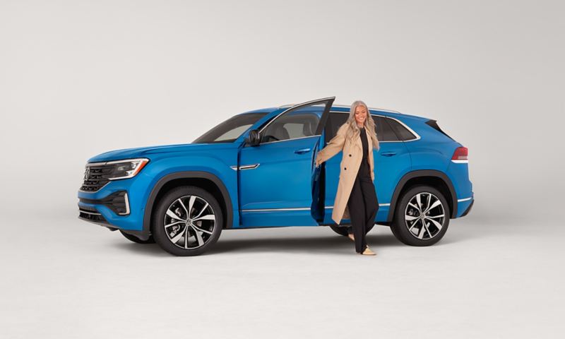 Person exiting an Atlas Cross Sport shown in Kingfisher Blue Metallic parked on a white background.