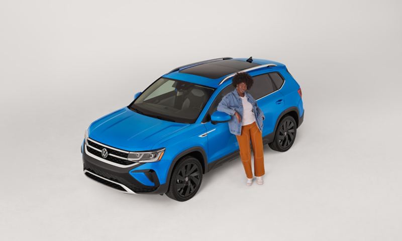 An overhead view of a Taos in Cornflower Blue parked on a white background with a person leaning on the driver door.