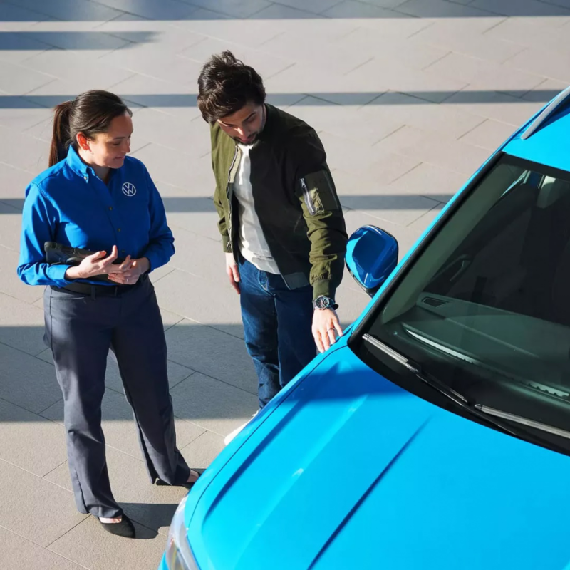 A VW dealership representative and a customer stand next to a VW SUV.