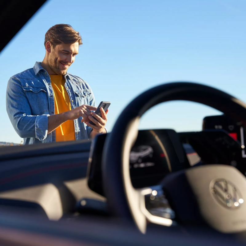 Looking through the windshield of a VW car at a man operating a smartphone.