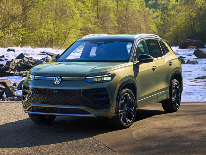 Front 3/4 view of a 2026 Tiguan in Avocado Green parked in front of a river with trees in background