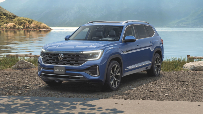 A 3/4 profile view of a Atlas shown in Mountain Lake Blue parked on a lake front with a view of the lake and grassy mountains in the background. 