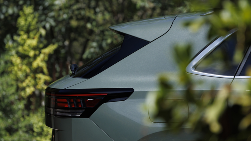Close up profile rear view of an Atlas Cross Sport shown in Dark Sage Metallic parked and slightly hidden behind some shrubbery.