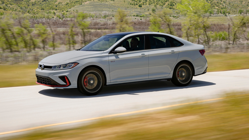 Jetta GLI shown in Monument Gray driving on a open road with wooded hills in the background