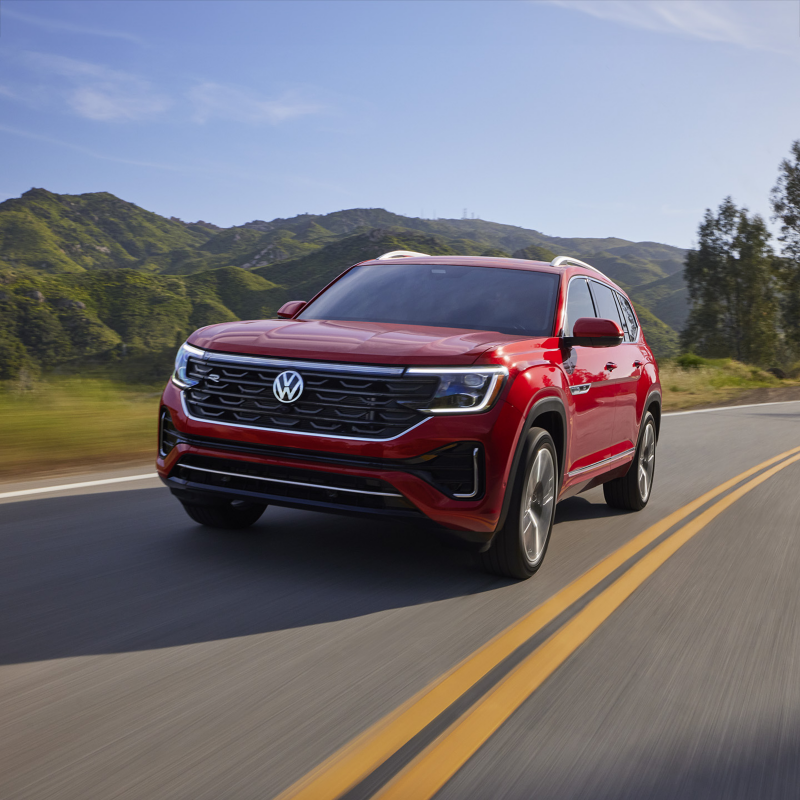 Atlas shown in Aurora Red Metallic seen from the front as it drives on a wooded mountain road.