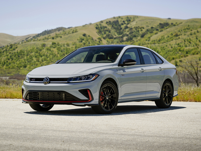 Front 3/4 view of a Jetta GLI shown in Monument Gray parked with a green hill with trees in the background