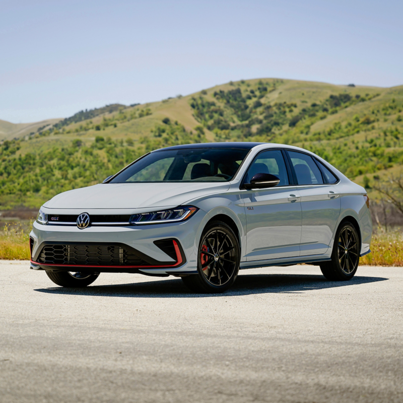 Front 3/4 view of a Jetta GLI shown in Monument Gray parked with a green hill with trees in the background