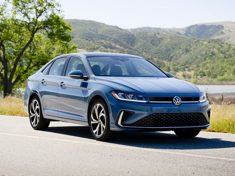 Vista frontal ¾ de un Jetta mostrado en Monterey Blue Pearl con colinas boscosas al fondo.