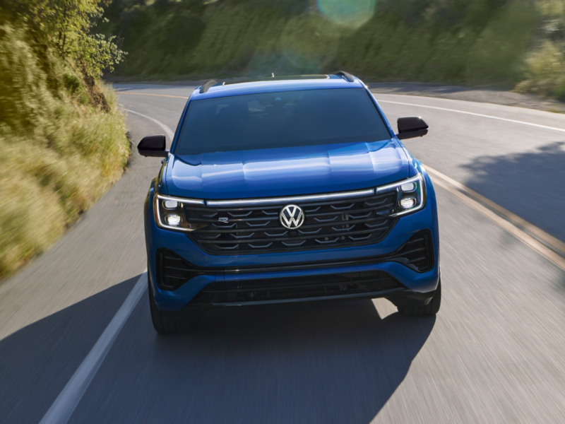 A front view of an Atlas Cross Sport shown in Mountain Lake Blue driving on a wooded mountain road.