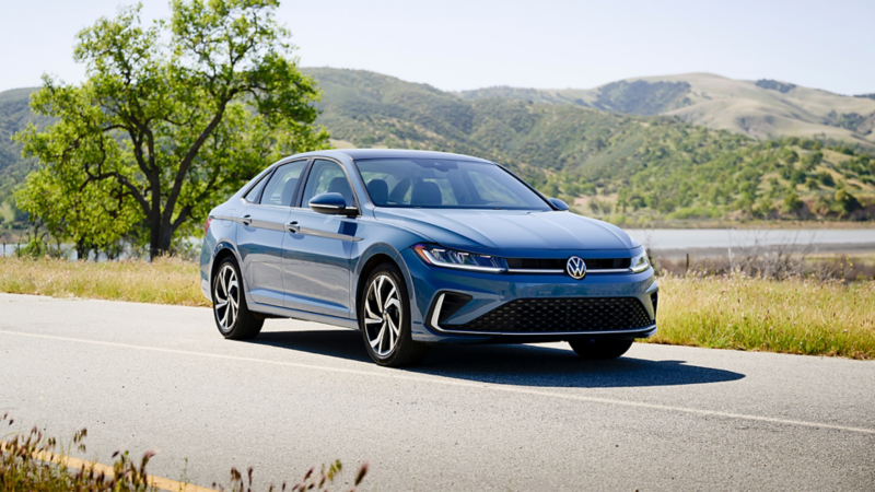 Front ¾ view of a Jetta shown in Monterey Blue Pearl parked on a road with wooded hills in the background