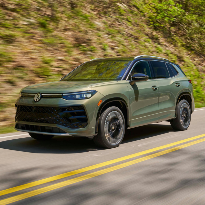 Front 3/4th view of a Tiguan shown in Avocado Green driving on a mountain road.