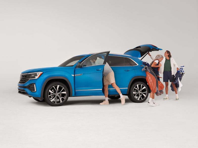 Three people exit an Atlas Cross Sport shown in Kingfisher Blue Metallic parked on a white background with golf equipment in hand.