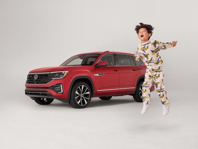 A child joyfully jumps outside an Atlas shown in Aurora Red Metallic parked on a white background.