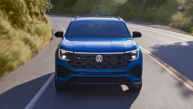 Head-on view of a Atlas Cross Sport driving on a mountain road with trees and shrubs making up the landscape.