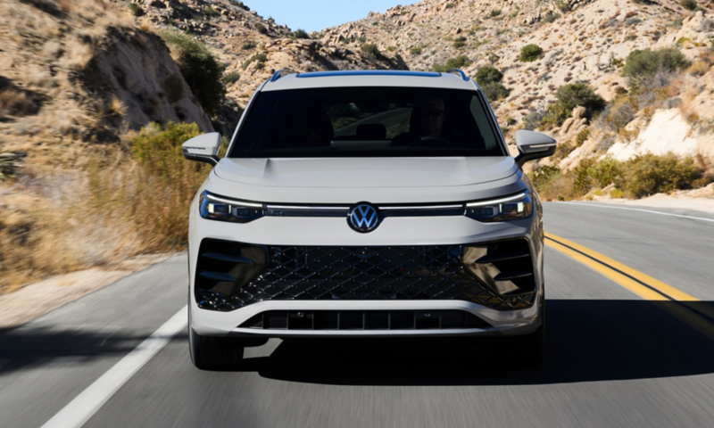 Head-on view of a Tiguan shown in Sandstone driving on a mountain road with rocks and shrubs making up the landscape.