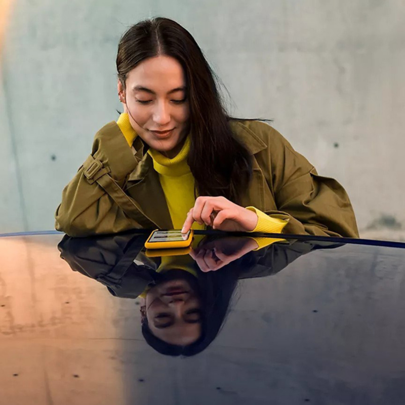 Una mujer vestida a la moda mira su teléfono inteligente.