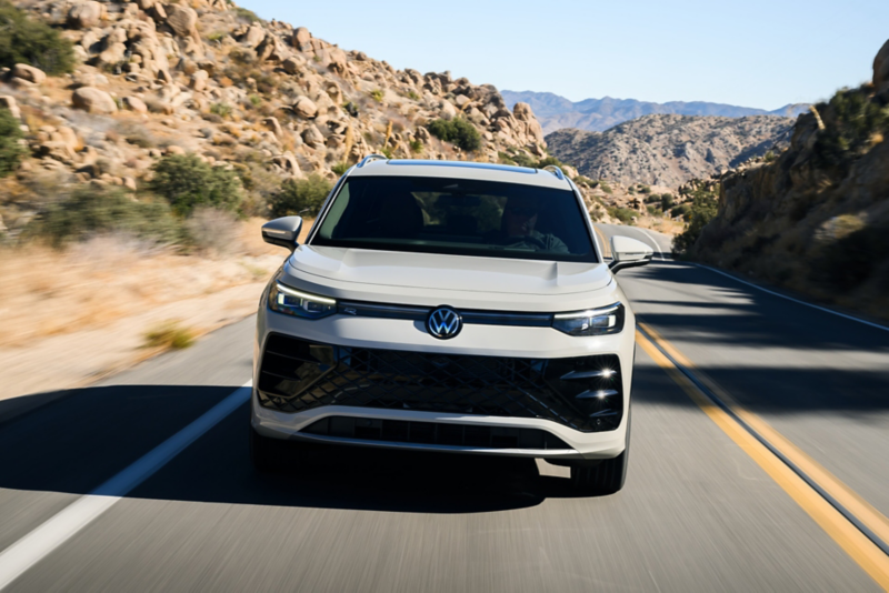 Head-on view of a Tiguan shown in Sandstone driving on a mountain road with rocks and shrubs making up the landscape.