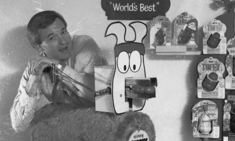 A black and white photo of a man operating a machine in front of dog toy display.