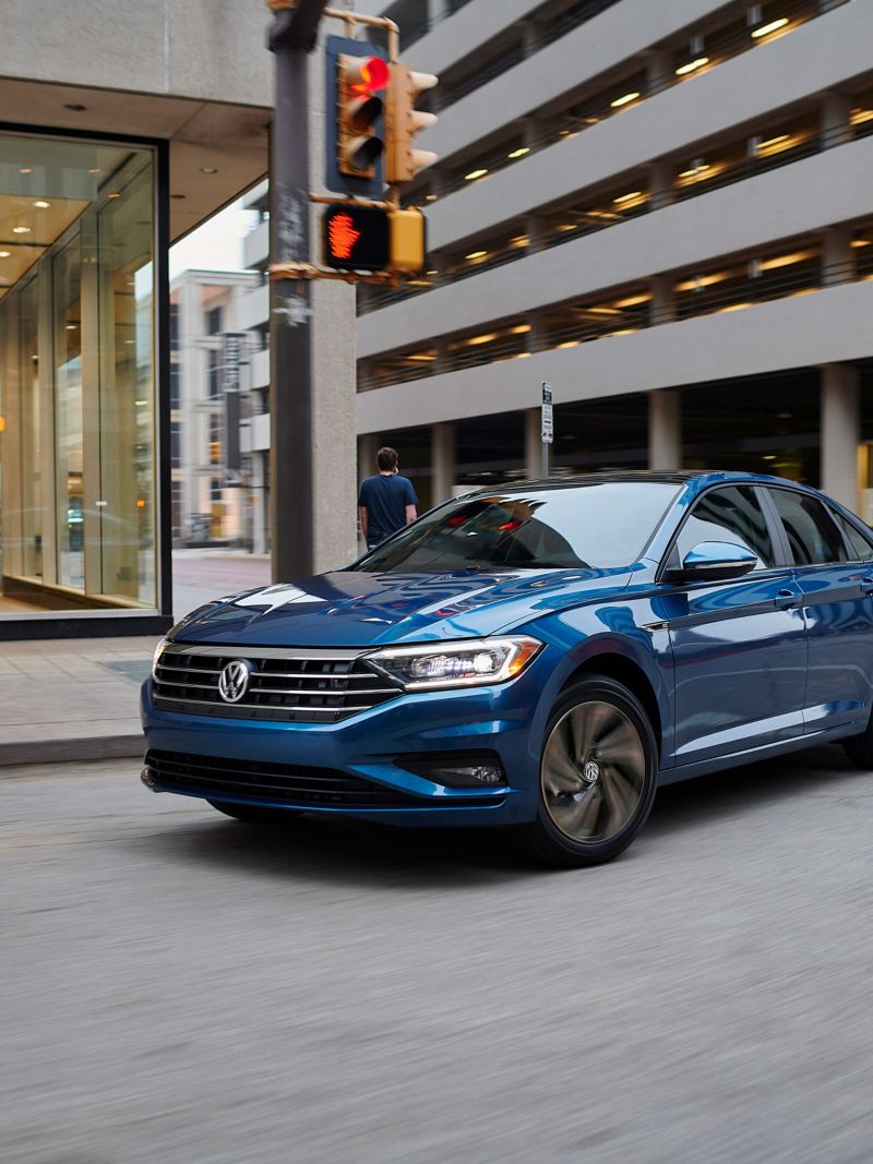 A tourmaline blue metallic Volkswagen Passat R-Line makes a right turn in the heart of a downtown street.