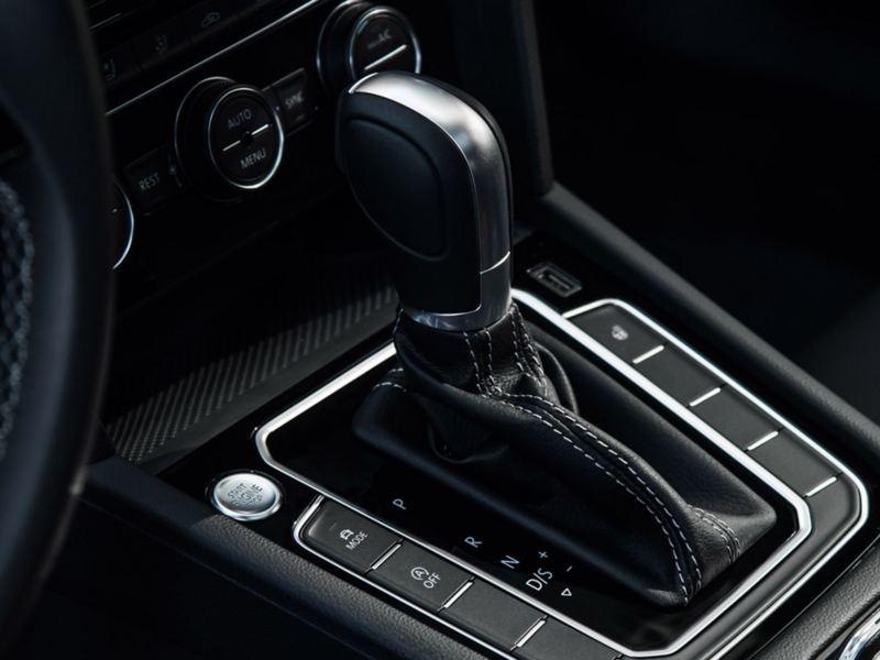 Toma del botón de arranque sin llave y del detalle decorativo color plata de la palanca de cambios recubierta con piel de color negro de un vehículo Volkswagen.