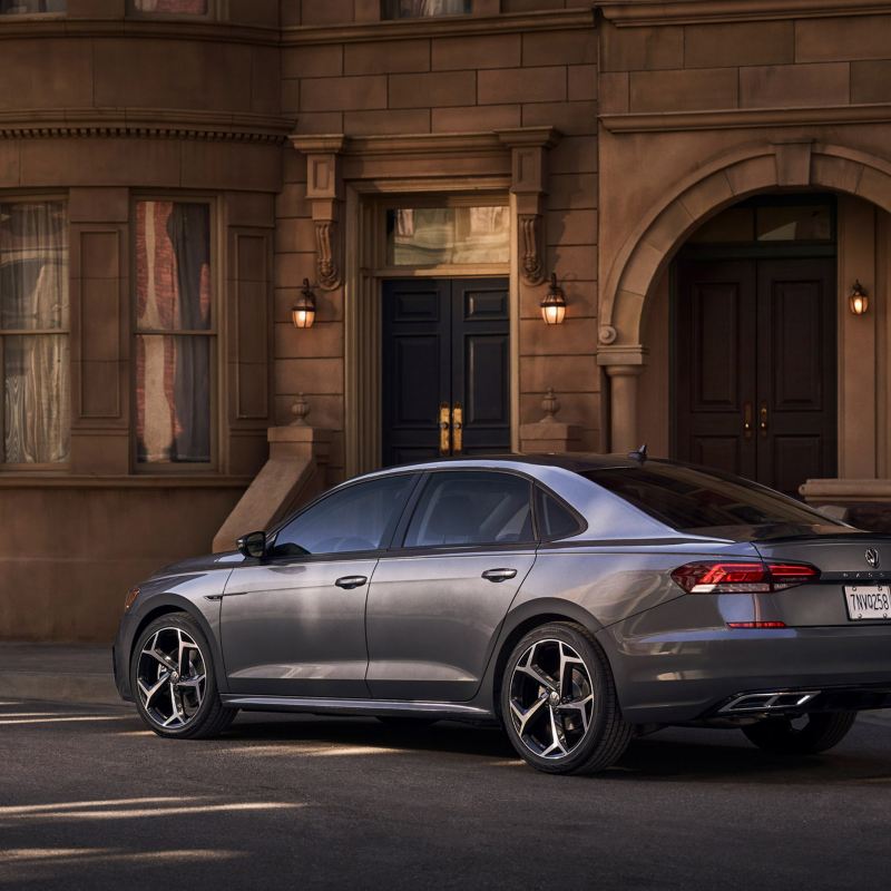 A platinum gray metallic Volkswagen Passat is parked off-street in front of neoclassical apartment building in early evening.