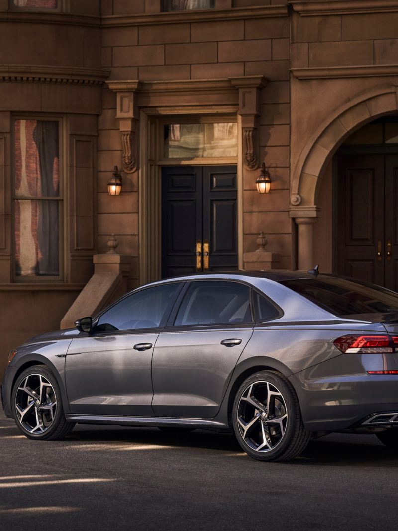 A platinum gray metallic Volkswagen Passat is parked off-street in front of neoclassical apartment building in early evening.