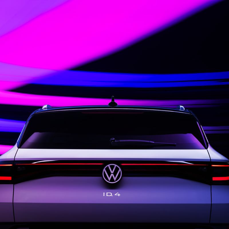 The brake lights of a VW ID.4 shown in Glacier White metallic are illuminated in the dark. Strokes of purple, pink and blue light add texture to the otherwise dark background.