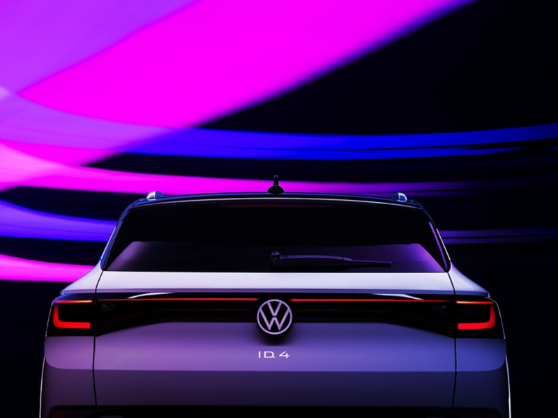 The brake lights of a VW ID.4 shown in Glacier White metallic are illuminated in the dark. Strokes of purple, pink and blue light add texture to the otherwise dark background.