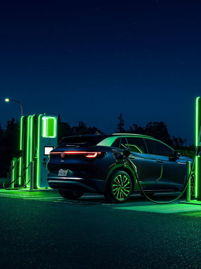 An ID.4 SUV in Tourmaline Blue Metallic is parked at night, charging at a neon lit charging station.