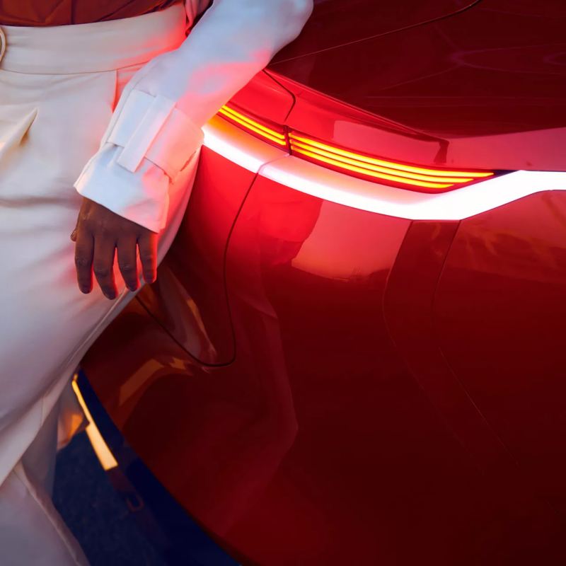 Mujer de moda de pie junto al vehículo eléctrico VW rojo.