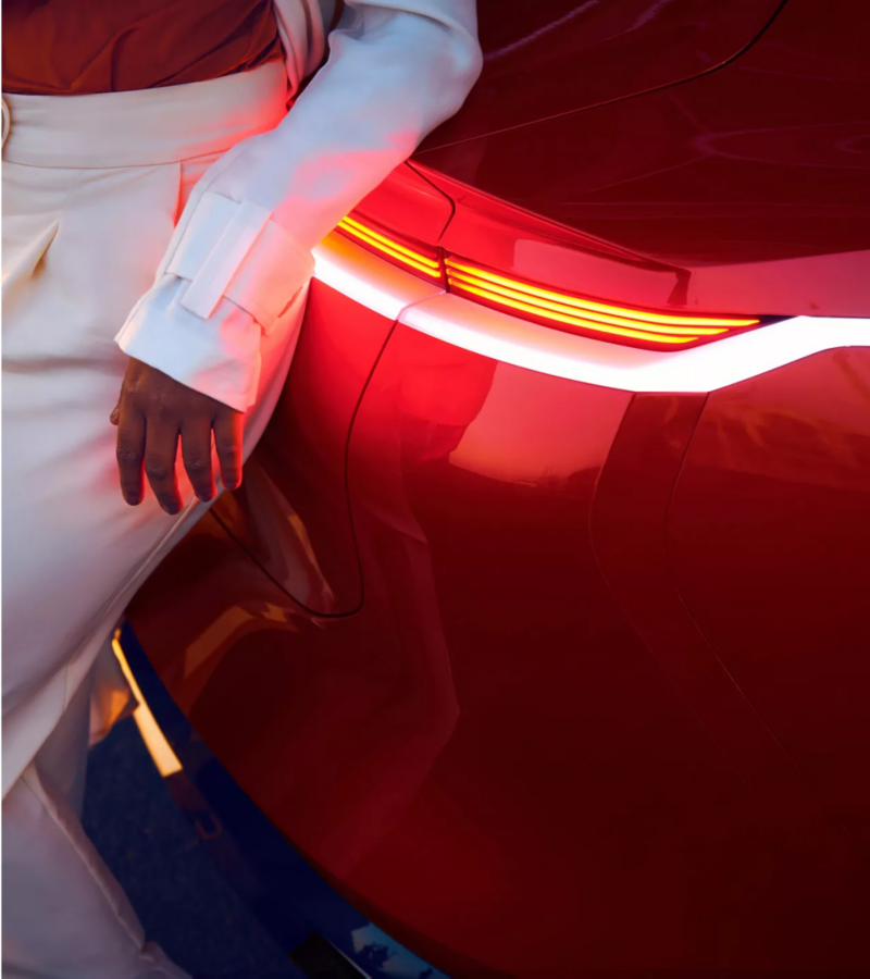 Fashionable woman standing next to red VW electric vehicle.