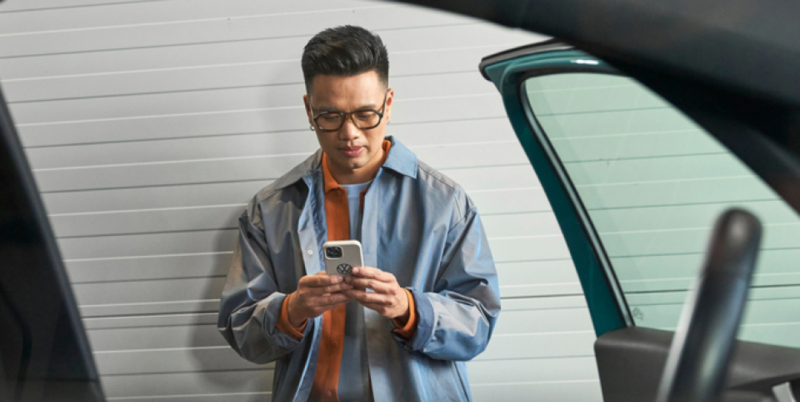 A young man opening his new car looking at his cell phone