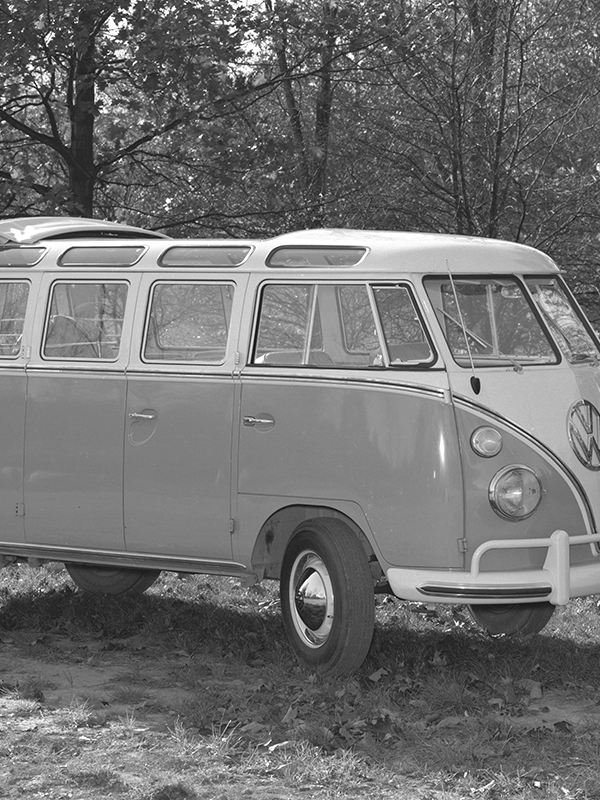 A black and white image of a vintage VW Bus in a park with trees and a picnic table in the background.