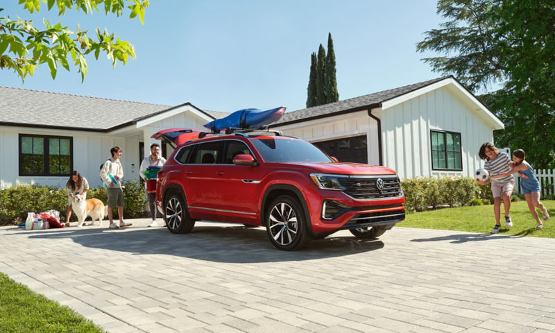 Atlas shown in Aurora Red Metallic parked in the driveway of a mid-century home with a family loading picnic goods in the rear and playing on the lawn nearby.