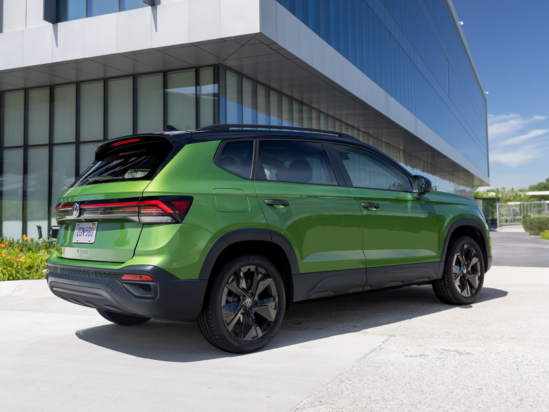 Low rear 3/4 view of a Taos shown in Bright Moss Green parked on in front of a modern architecture building.