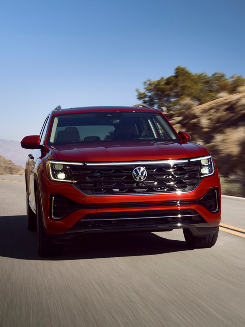 Atlas shown in Aurora Red Metallic seen from the front as it drives on a wooded mountain road.