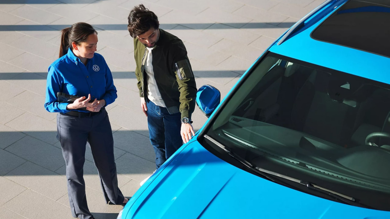 A VW dealership representative and a customer stand next to a VW SUV.