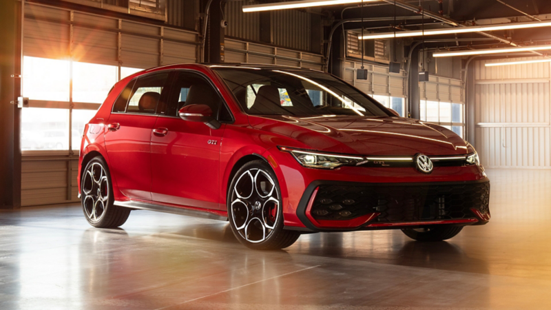 Three-quarter front view of a Kings Red Metallic Golf GTI parked in a sunlit parking garage with architectural shadows.