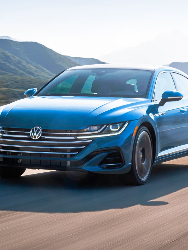 An Arteon shown in Kingfisher Blue Metallic drives along a road with foothills in the background.