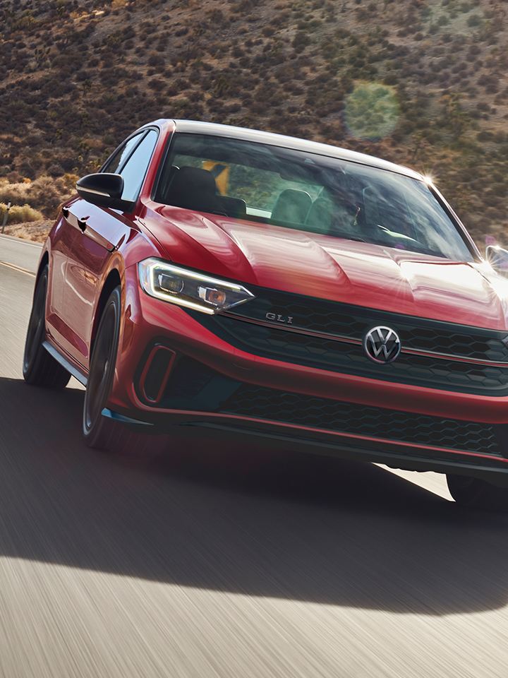 A front view of the Jetta GLI shown in Kings Red Metallic driving on a road with a mountain in the background.