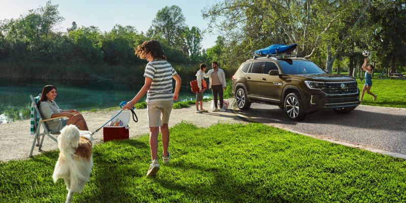 Atlas shown in Avocado Green Metallic parked in a park with a family carrying picnic goods near the rear and playing on the lawn nearby.