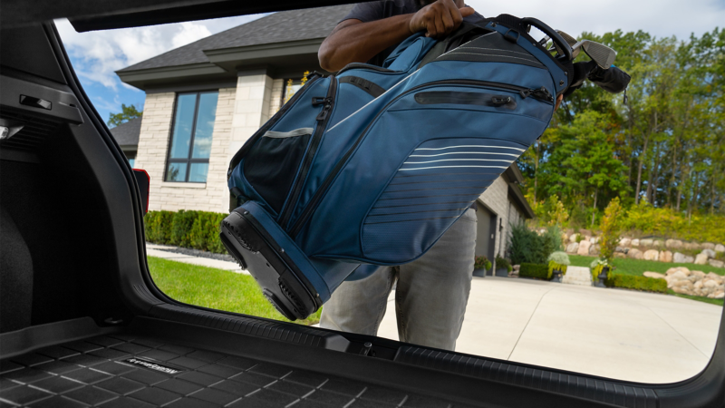 Golf clubs being loaded into the trunk of a vehicle protected by a MuddyBuddy trunk liner
