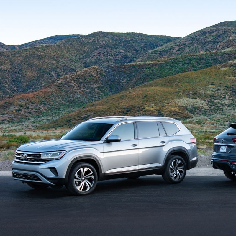 The 2021.5 Atlas and 2020 Atlas Cross Sport parked in front of mountains, showing front 3/4 and rear 3/4 views respectively.