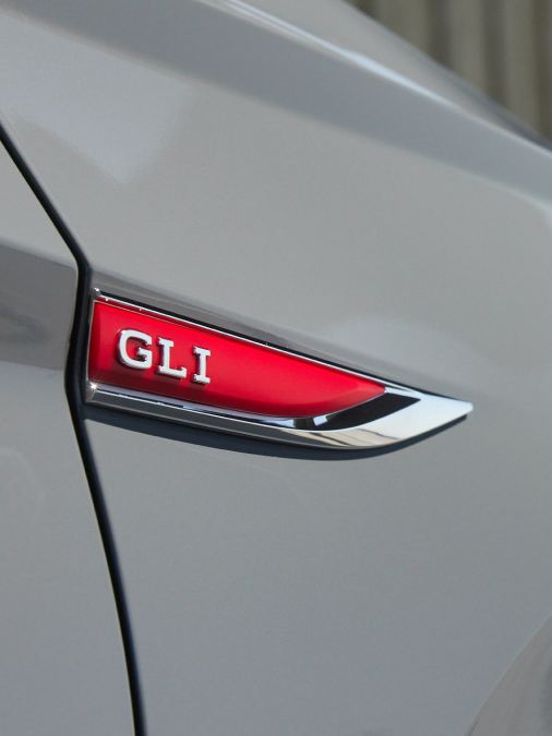 Primer plano del emblema GLI en el guardabarros delantero derecho del VW Jetta GLI Pure Gray. El color eleva el precio de $395.