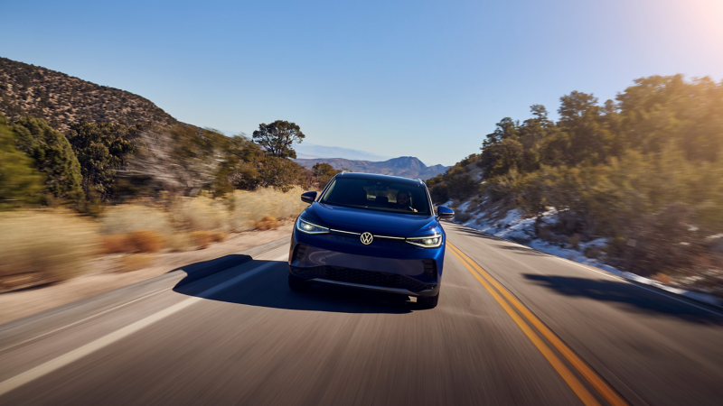 Front-end view of a 2021 Volkswagen ID.4 driving down a two-lane highway with mountains in the background. 