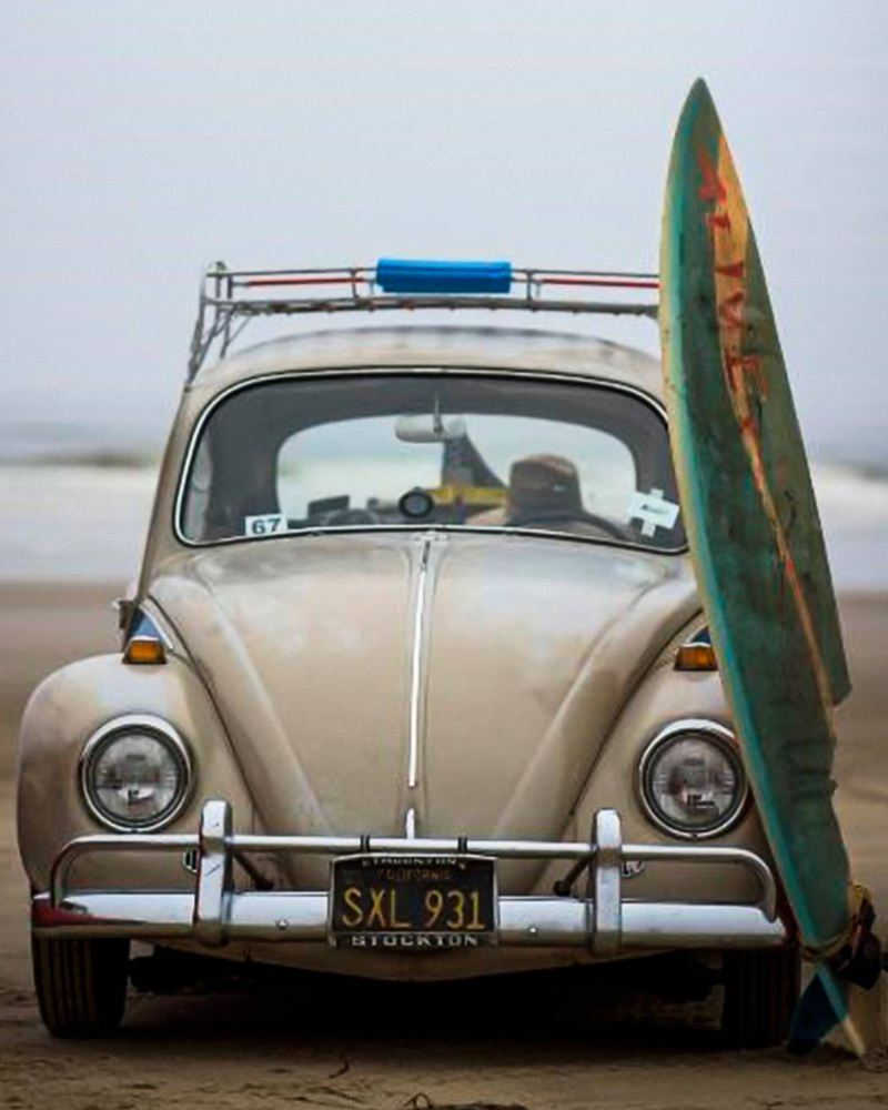 Volkswagen Beetle vintage estacionado junto a la playa con una tabla de surf