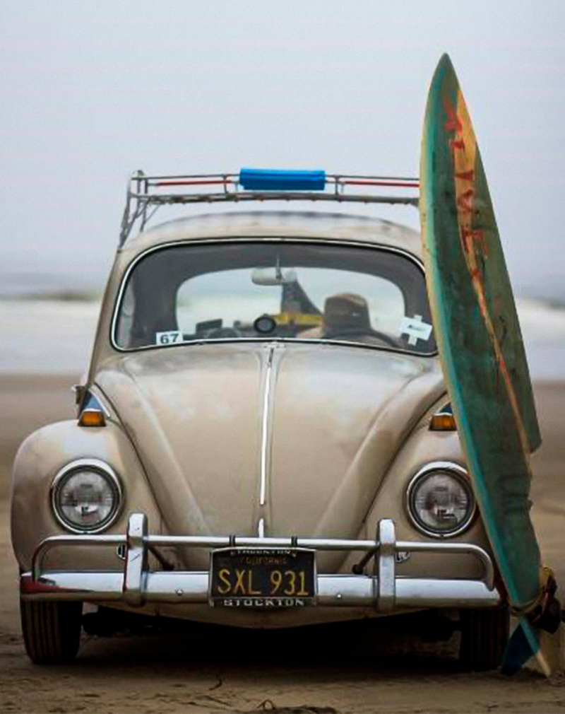 Vintage Volkswagen Beetle parked by the beach with a surfboard