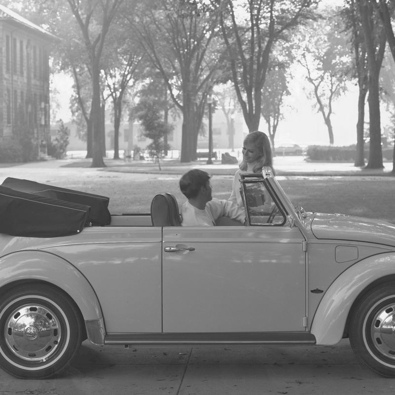 Un joven que conduce un Volkswagen Beetle convertible 1969, se detuvo a hablar con una joven en un campus universitario.